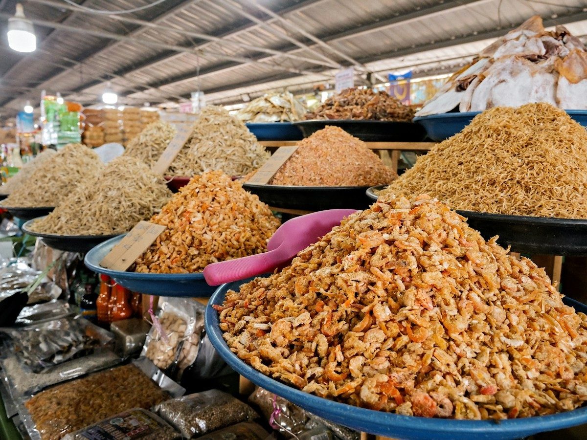 Étal de marché couvert de grands plateaux de crevettes séchées et de petits poissons