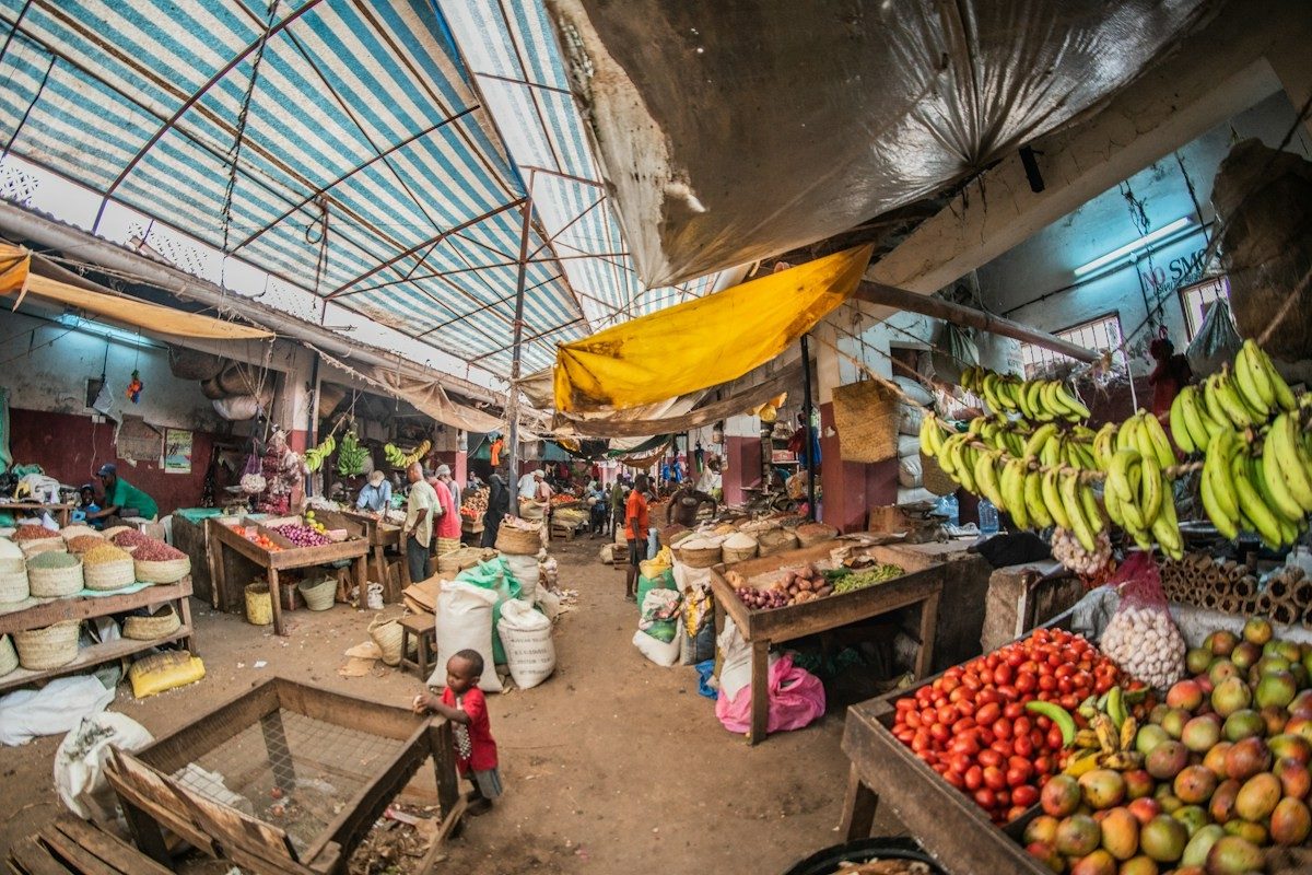 Allée d'un marché couvert, avec des régimes de bananes et des étals de fruits de part et d'autre