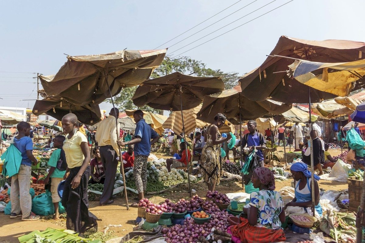 Marché en plein air sous de grands parasols, avec vendeurs et acheteurs
